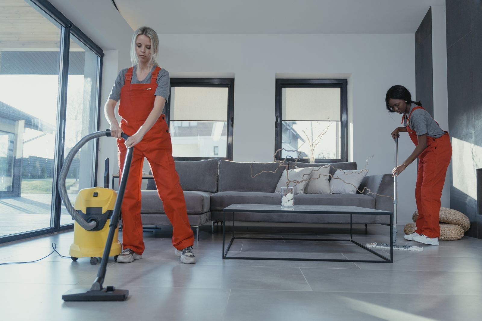 Professional cleaner in workwear vacuuming and mopping an open-plan office
